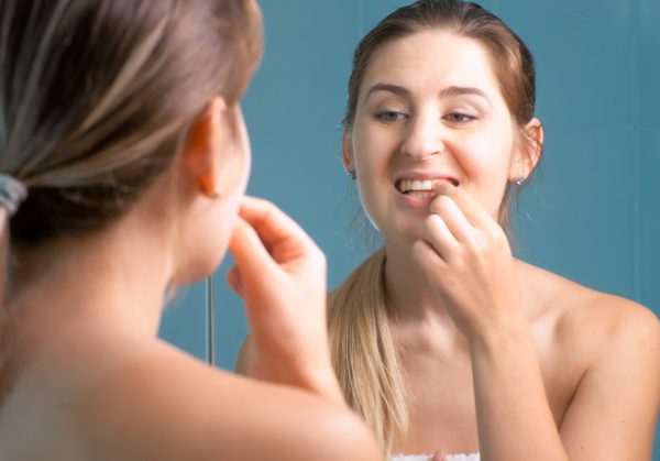 Young woman cleaning and checking her teeth at mirror in bathroom.