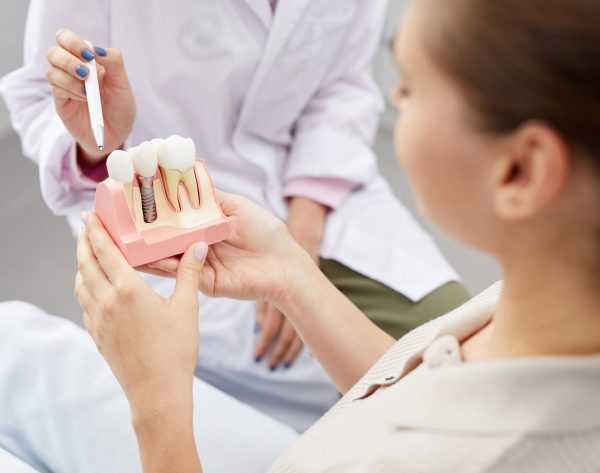 Closeup of unrecognizable female doctor pointing at tooth model while consulting patient, copy space